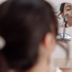 Kobieta wykonuje delikatny makijaż pędzlem przed małym lusterkiem