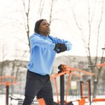 Sportowiec w niebieskiej bluzie rozgrzewa się na zewnętrznej siłowni zimą
