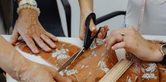 Dwie osoby wycinają nożyczkami kwiatową tkaninę w pracowni krawieckiej